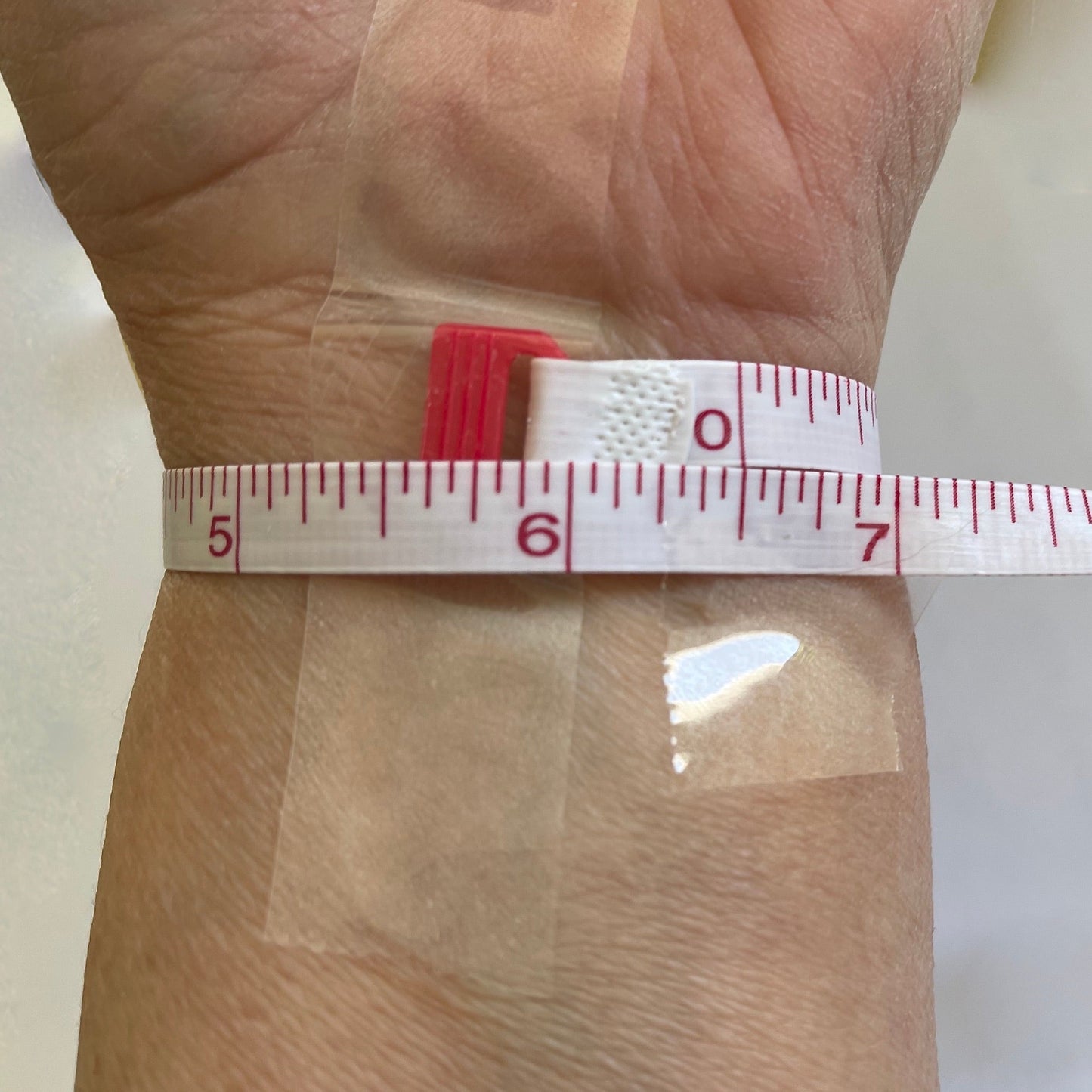 Use Soft Tape Measure to Measure Wrist right under hand. Designer has a 6.5" wrist.